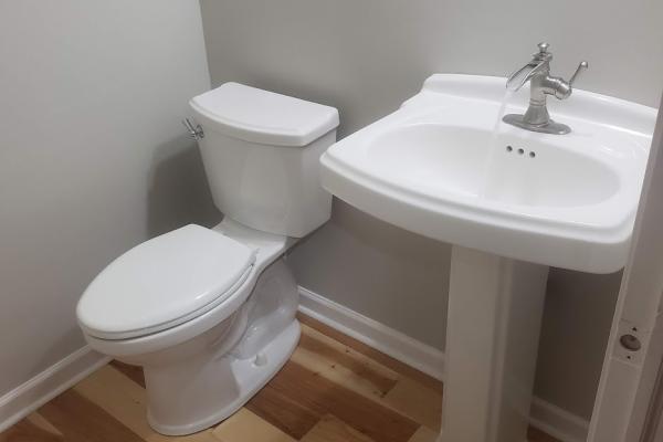 A stylish half bathroom renovation featuring a white porcelain pedestal sink with a waterfall faucet and a modern close coupled toilet. Expert plumbing solutions in Tatamy, PA, offer insights into upgrading bathroom fixtures for enhanced comfort and style. Applause Plumbing can design your bathroom remodel today!