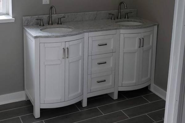 Double sink marble vanity with white cabinet doors, expertly installed by Applause Plumbing and Heating.  Applause Plumbing transforms outdated spaces into beautiful, functional havens. Meticulous attention to detail, upgraded plumbing fixtures, and thoughtful lighting create a warm, inviting atmosphere. Trust us to bring your bathroom dreams to life with professionalism, reliability, and a commitment to customer satisfaction.