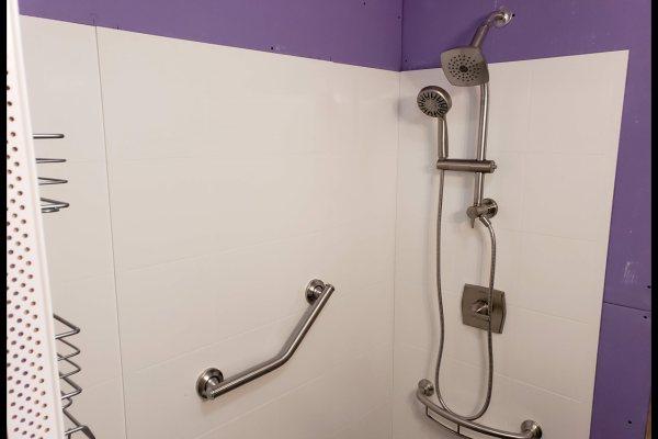 A beautifully remodeled bathroom featuring a spacious walk-in shower with a sleek shower head, wand, and grab bar that was completed by Applause Plumbing in Stewartsville, New Jersey. The shower niche neatly holds shampoo and soap bottles, creating a luxurious and accessible bathing space.