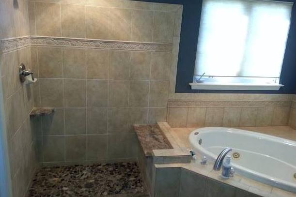 A luxurious custom-built master bathroom showcasing a separate bathtub and shower arrangement. The bathtub, adorned with elegant tile surroundings, invites relaxation with its deep soaking design. Custom lighting fixtures illuminate the space, creating a serene ambiance for unwinding and rejuvenation. This project was completed by Applause Plumbing and Heating for a customer in Forks, Pennsylvania.
