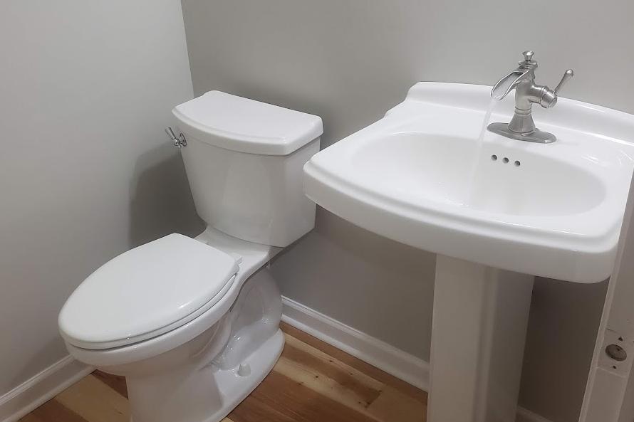 A stylish half bathroom renovation featuring a white porcelain pedestal sink with a waterfall faucet and a modern close coupled toilet. Expert plumbing solutions in Tatamy, PA, offer insights into upgrading bathroom fixtures for enhanced comfort and style. Applause Plumbing can design your bathroom remodel today!