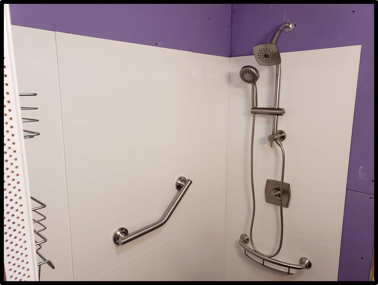 A beautifully remodeled bathroom featuring a spacious walk-in shower with a sleek shower head, wand, and grab bar that was completed by Applause Plumbing in Stewartsville, New Jersey. The shower niche neatly holds shampoo and soap bottles, creating a luxurious and accessible bathing space.